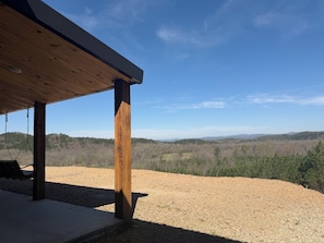 Ein überdachter Außenbereich mit einer Schaukel, einem Holzmast und Blick auf eine hügelige Landschaft.