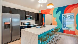 A modern kitchen with stainless steel appliances, a marble island, and bar stools. - The EaDo Compound: Main house + Guest House (Houston)