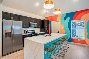 A modern kitchen with stainless steel appliances, a marble island, and bar stools. - The EaDo Compound: Main house + Guest House (Houston)
