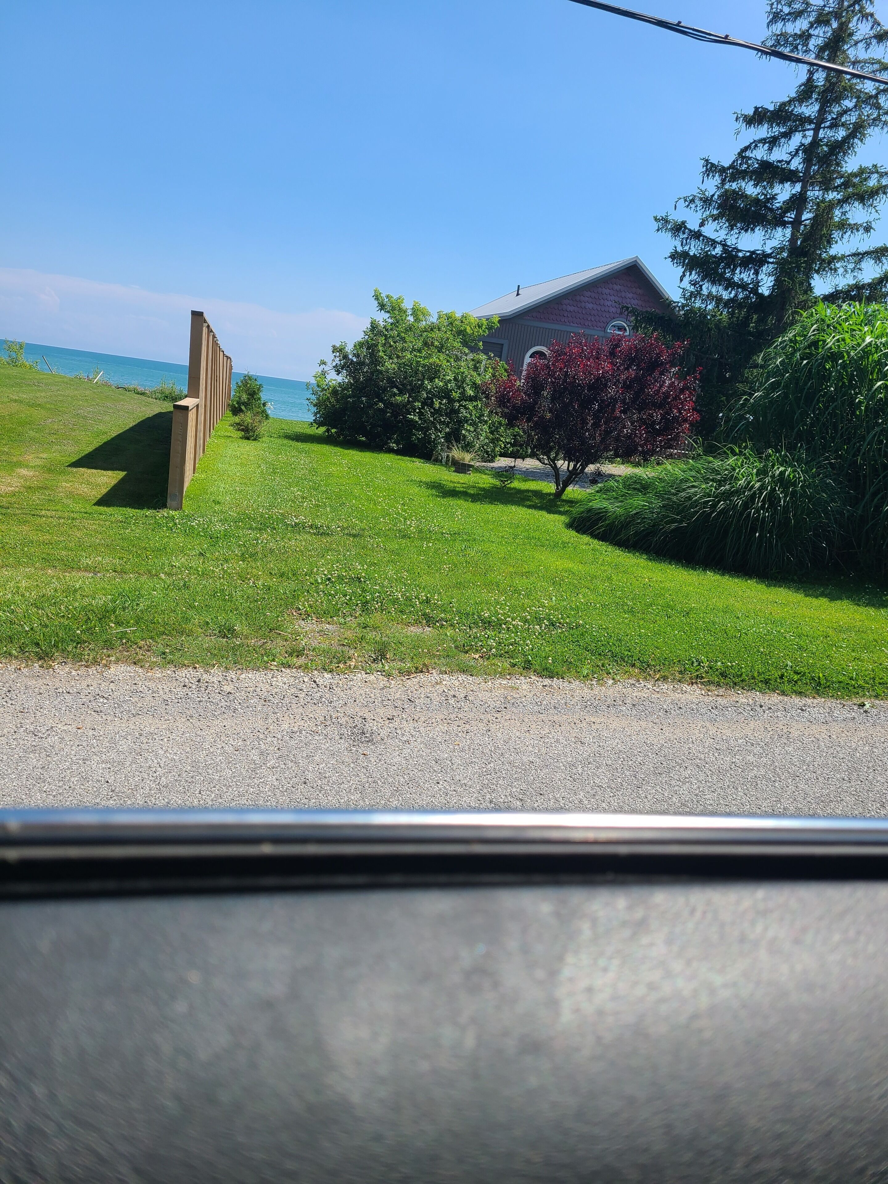 A grassy area with a building, a tree, and a view of the sea.