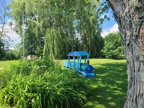 A small blue train in a park with lush greenery and trees.