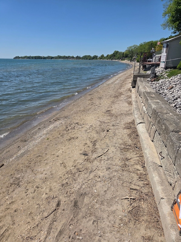 A sandy beach with a stone wall and a building with a flag.