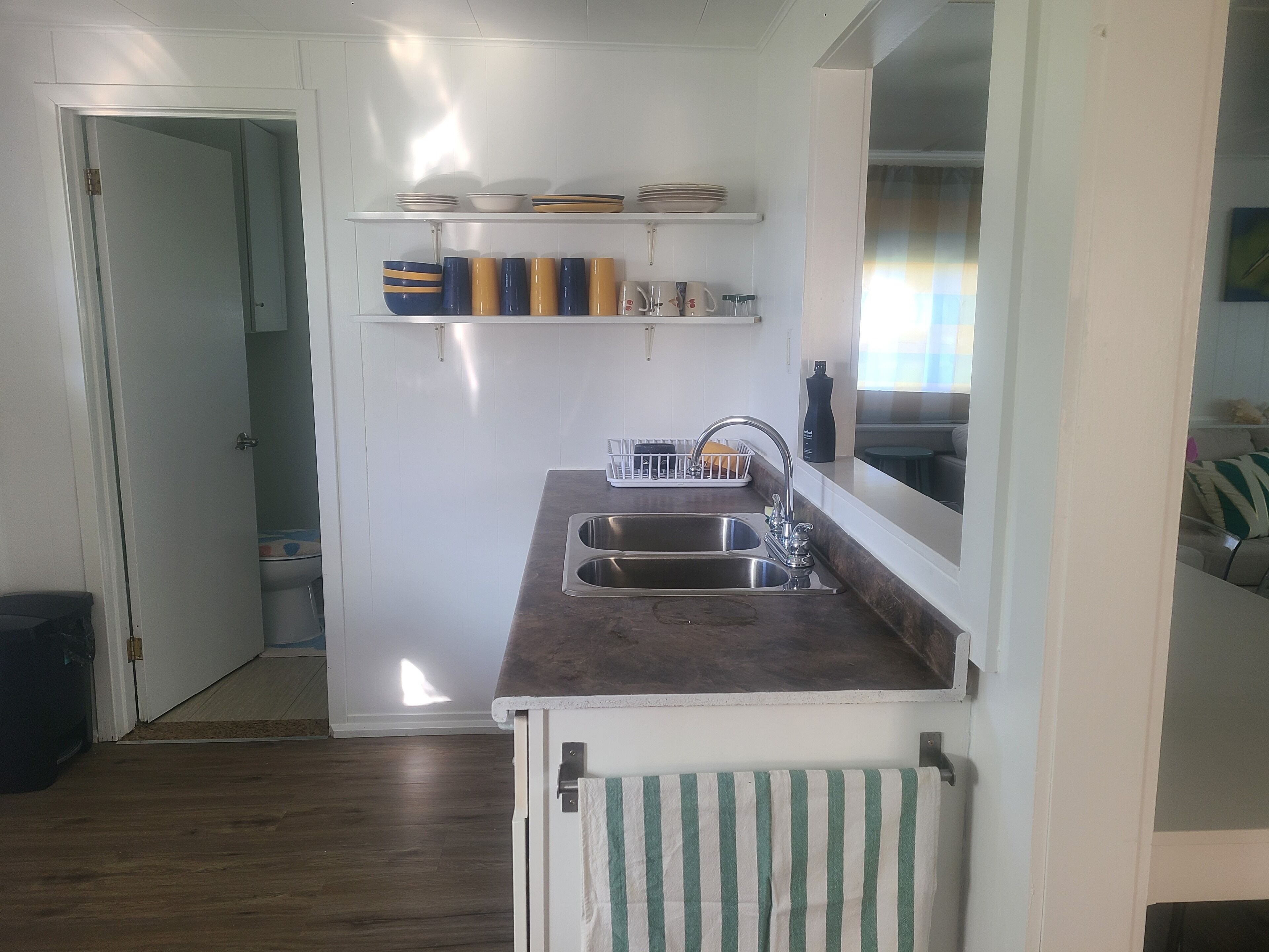 A compact kitchen with a sink, a window, and a door leading to a bathroom.