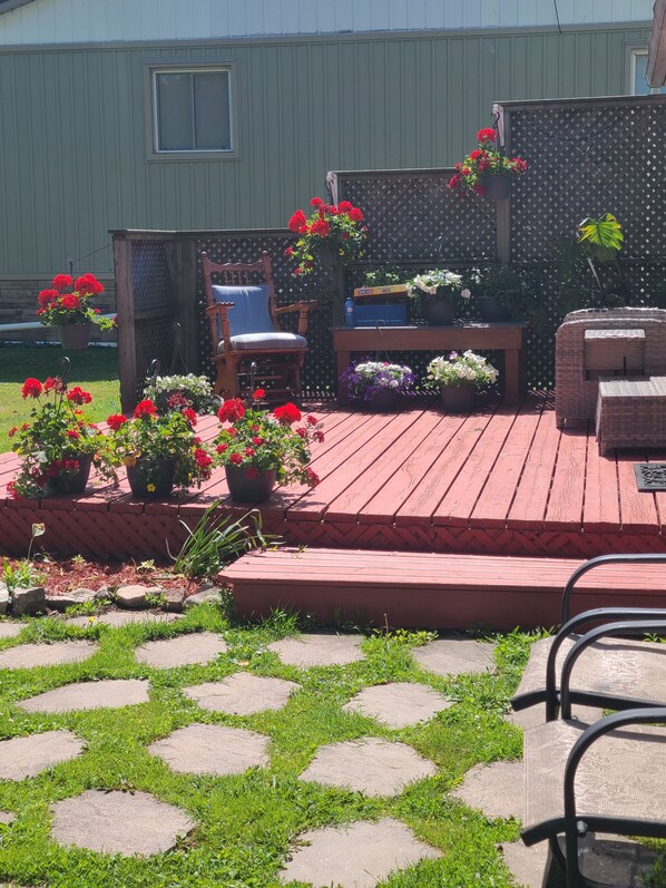 A wooden deck with potted plants, a chair, and a table.