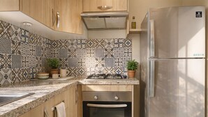 Cocina compacta con gabinetes de madera, estufa a gas, horno empotrado y refrigerador de acero inoxidable.