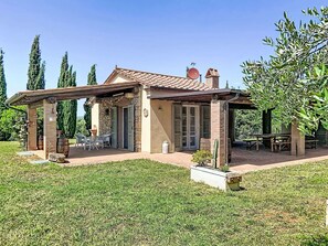 Ein Haus mit Terrasse, Steinpfeilern, einer überdachten Sitzgruppe und einem Garten.