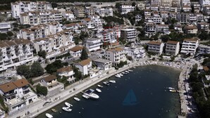 Vista aerea di una cittadina costiera con edifici residenziali, un porto turistico con barche e una limpida visuale sul mare.
