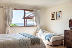 A bedroom with two beds, a window with curtains, a dresser, and two framed pictures on the wall. - Views, Beaches, Barbeques and more at Tom's Cabin: 3 Bedrooms, Sleeps 6 (Cape Town)