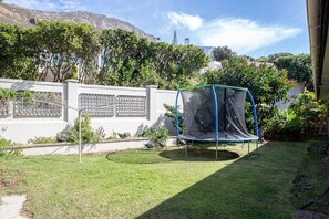 A backyard with a trampoline, a white fence, and a mountain in the background. - Views, Beaches, Barbeques and more at Tom's Cabin: 3 Bedrooms, Sleeps 6 (Cape Town)