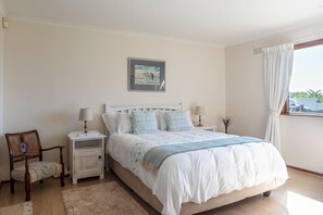 Une chambre à coucher comprenant un lit, deux tables de chevet, une chaise, un tableau au mur et une fenêtre avec des rideaux.