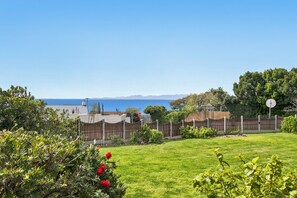 A grassy yard with a wooden fence, a stop sign, and a view of the sea and mountains in the background. - Views, Beaches, Barbeques and more at Tom's Cabin: 3 Bedrooms, Sleeps 6 (Cape Town)