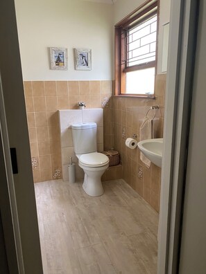A bathroom with a toilet, sink, and two framed pictures on the wall. - Views, Beaches, Barbeques and more at Tom's Cabin: 3 Bedrooms, Sleeps 6 (Cape Town)