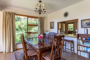 A dining room with a large wooden table, chairs, a chandelier, and a view of the outdoors.