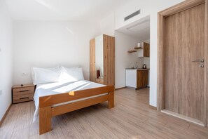 Un dormitorio con una cama de madera, una mesita de noche, un escritorio pequeño, un armario y una cocina con un fregadero y muebles.