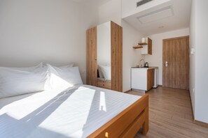 A bedroom with a bed, a wooden bench, a small kitchenette, and a door leading to another room. - Cozy apartment 3 with sea view (Neum)