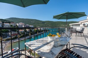 A terrace with a table, chairs, and a view of a river and buildings. - Cozy apartment 3 with sea view (Neum)