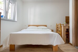 A neatly made bed in a room with a wooden floor, a window, and a wooden chair. - Comfortable studio apartment 6 (Neum)