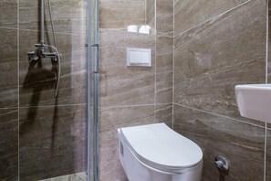 A bathroom with a shower, toilet, and a wall-mounted light fixture. - Comfortable studio apartment 6 (Neum)