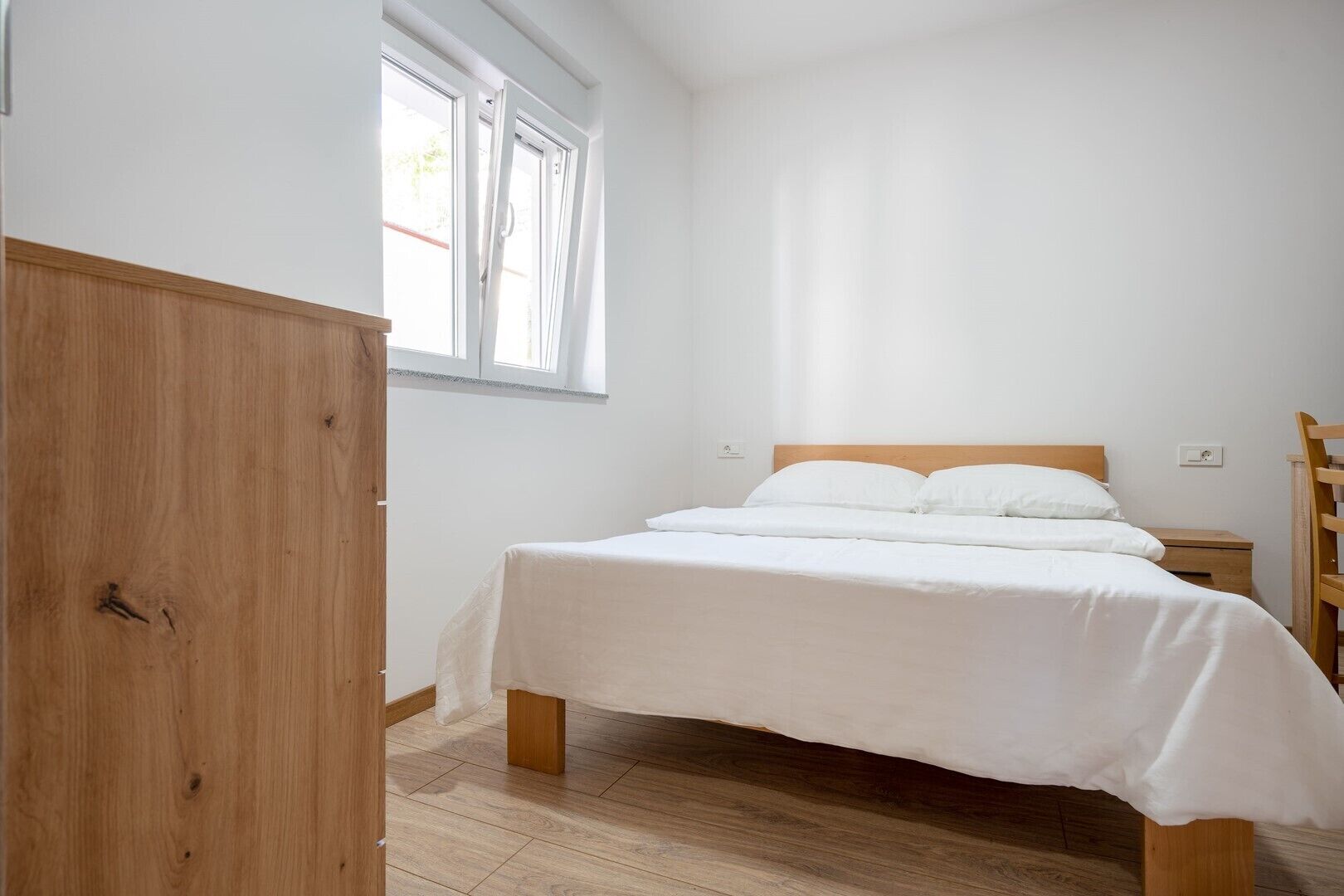 Een slaapkamer met een houten bed, een houten kledingkast en een raam met gordijnen.