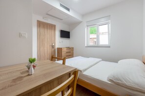 A bedroom with a wooden bed, a bedside table, a TV mounted on the wall, and a window with a view of greenery. - Comfortable studio apartment 6 (Neum)