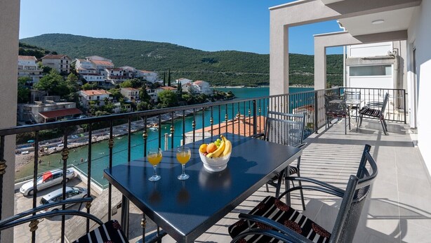 Ein Balkon mit Tisch, Stühlen und Blick auf eine Küstenstadt und das Meer.