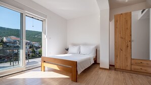 Ein Schlafzimmer mit einem Bett, einem Holzschrank und einem großen Fenster mit Blick auf eine Hügellandschaft.