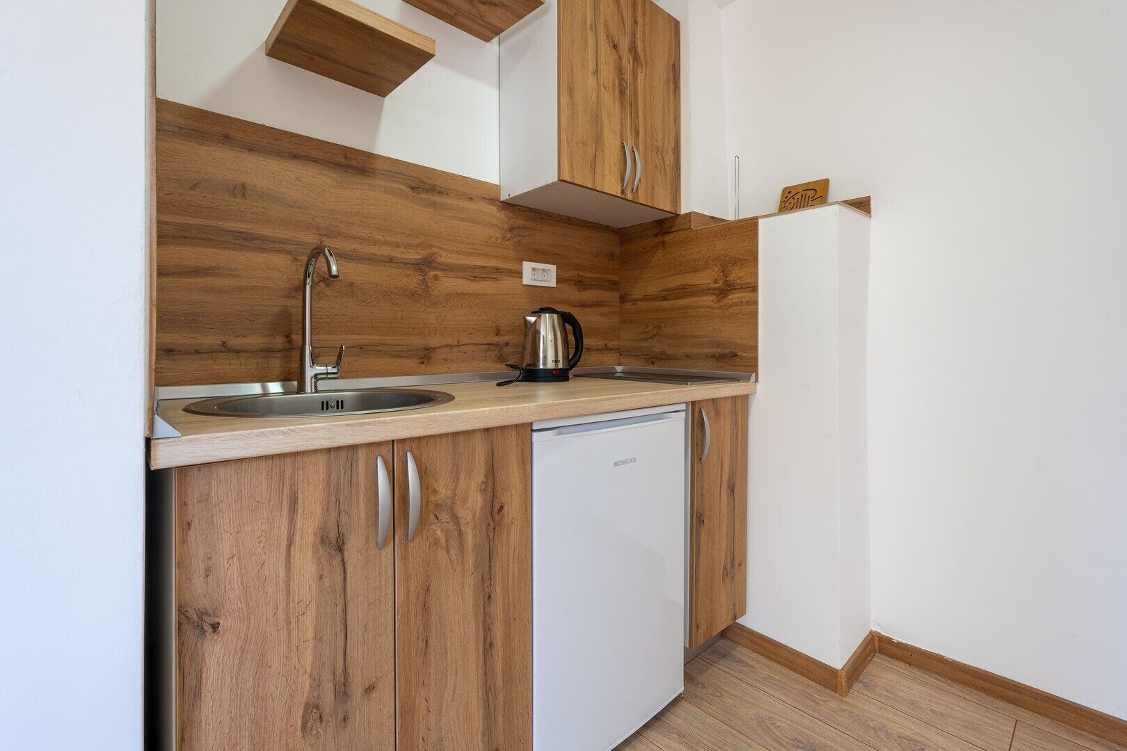Una cucina compatta con mobili in legno, un lavello in acciaio inossidabile, una macchina da caffè e una lavastoviglie bianca.