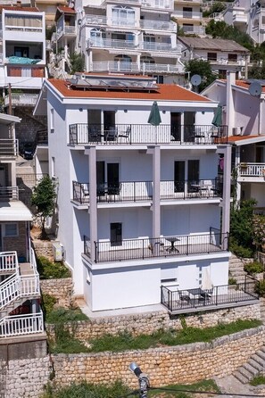 A multi-story building with balconies, outdoor seating, and a stone retaining wall. - Sea view apartment 9 (Neum)