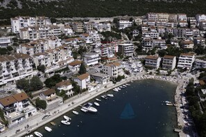 Vista aerea di una cittadina costiera con edifici residenziali, un porto turistico con barche e una limpida visuale sul mare.