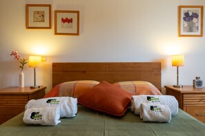 Une chambre d’hôtel avec une tête de lit en bois, deux lampes de chevet, un couvre-lit vert, deux oreillers et deux serviettes ornées d’un logo.