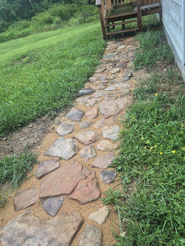 Un chemin de pierres menant à une structure en bois, le tout entouré de verdure.