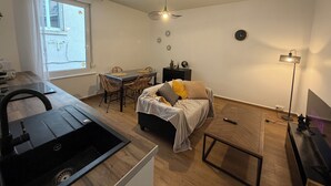 Een knus kamertje met een bed, een eettafel, een kitchenette en een raam met uitzicht.