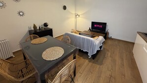 Een knus woongedeelte met een eettafel, stoelen, een bank, een televisie en een plafondlamp.