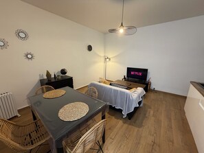 A compact living space with a dining table, chairs, a sofa, a TV, and a ceiling light fixture. - Apartment 5 minutes from the station (Metz)