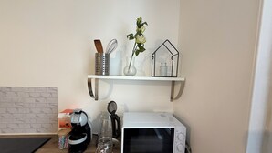 Een keuken met een magnetron, koffiezetapparaat en een plank met keukengerei en een vaas.