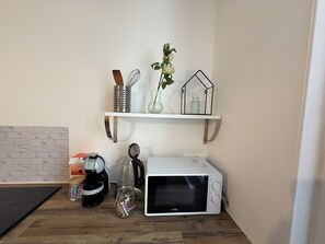A kitchen with a microwave, coffee maker, and a shelf with kitchen utensils and a vase. - Apartment 5 minutes from the station (Metz)