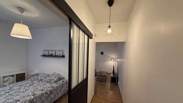 Een moderne slaapkamer met een bed, een hanglamp, een plank met boeken en uitzicht op een andere kamer.