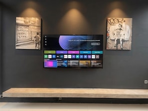 Ein Flachbildfernseher an einer dunklen Wand, darunter ein Holzregal.