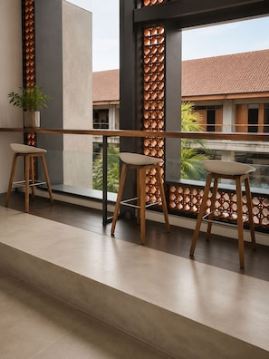 Ein modernes Interieur mit Balkon, zwei Holzschemeln, einer Topfpflanze und Blick auf ein Gebäude mit Ziegeldach.