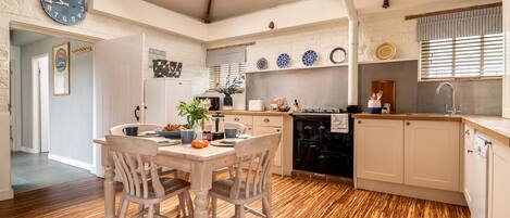 Una cocina con piso de madera, una mesa de comedor con sillas, un reloj y una ventana con persianas.
