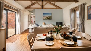 Un comedor con una mesa de madera preparada para el desayuno, una pared de ladrillo y un ventanal con cortinas.