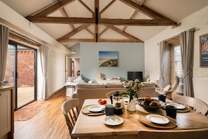 Un coin repas avec une table en bois mise pour le petit-déjeuner, un mur en briques et une grande fenêtre avec des rideaux.