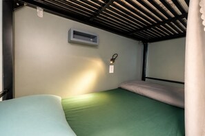 Uma cama beliche com colchão verde, um ar-condicionado fixado na parede e uma tomada.
