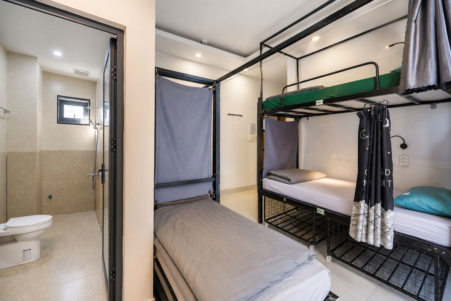 A compact room with a shower, a toilet, and two bunk beds with curtains.