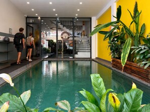 Un espace piscine doté d’un mur en verre, de plantes d’intérieur et d’un escalier menant à un deuxième étage.