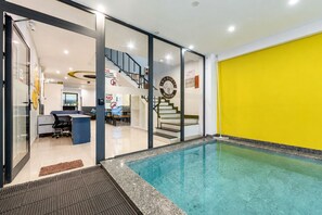 Interior de hotel com piscina, balcão de recepção e escada que leva a um andar superior.