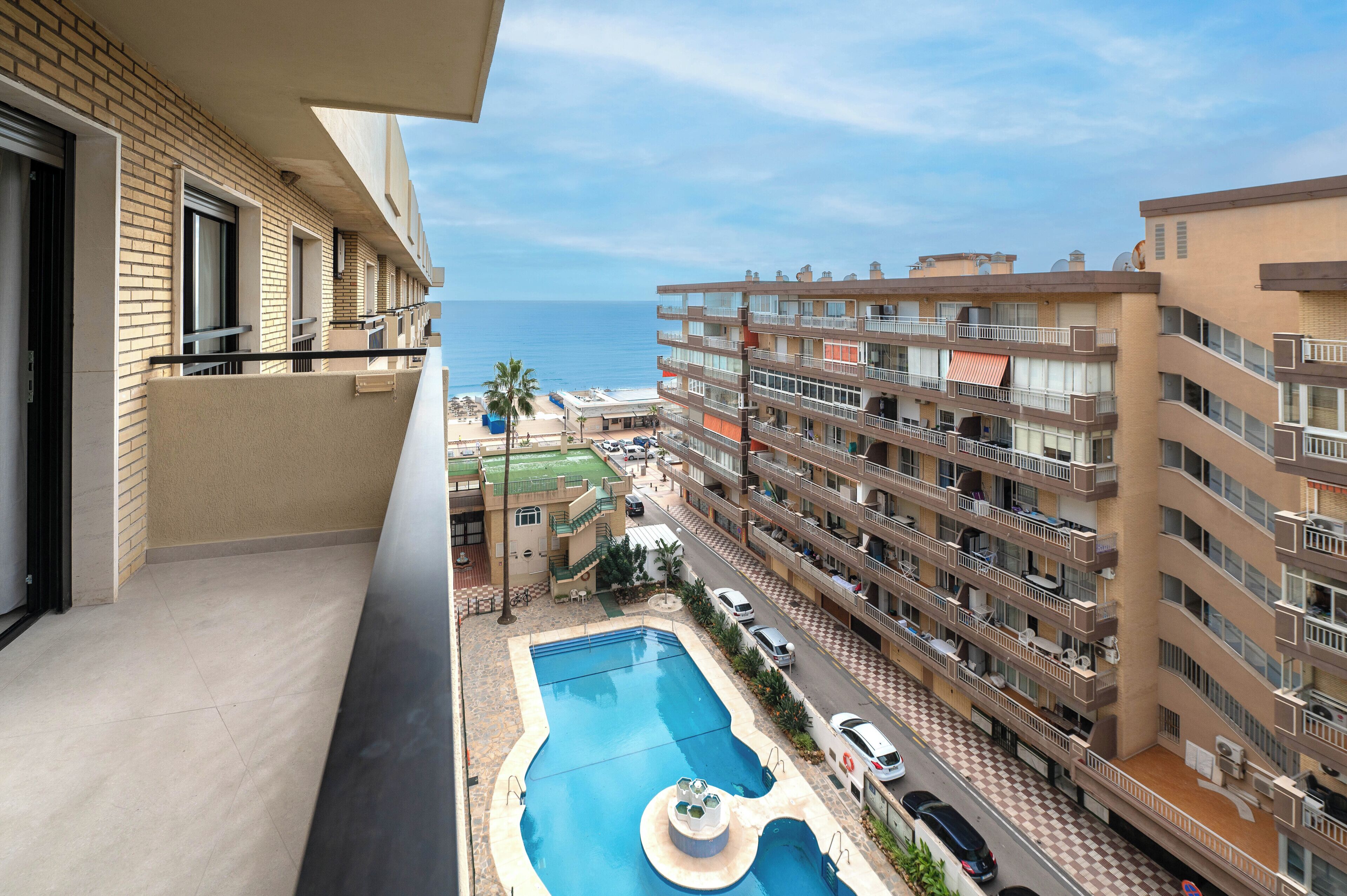A multi-story building with a swimming pool, balconies, and a view of the sea.