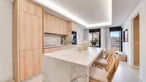 A modern kitchen with wooden cabinets, a marble countertop, and a dining area with chairs. - LXR Dalí 1-Bedroom Beachfront (Fuengirola)