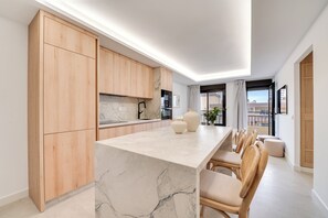 A modern kitchen with wooden cabinets, a marble countertop, and a dining area with chairs. - LXR Dalí 1-Bedroom Beachfront (Fuengirola)