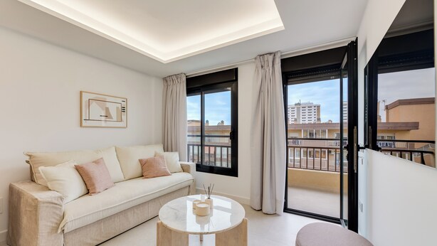 A modern living room with a sofa, a coffee table, and a view of a balcony with buildings. - LXR Dalí 1-Bedroom Beachfront (Fuengirola)